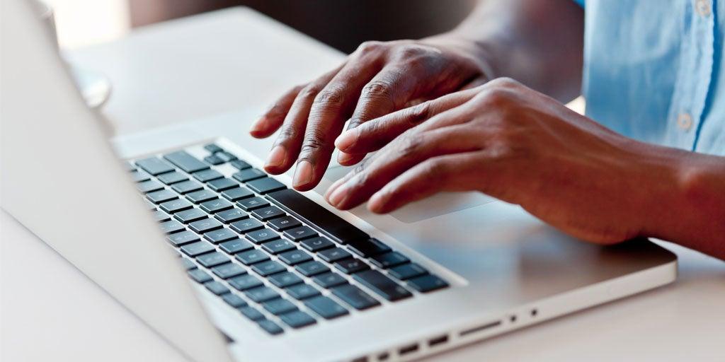 A close up shot of a Black person typing on a laptop.