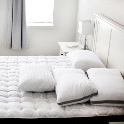 A clean white bedroom with a bed and pillows without sheets
