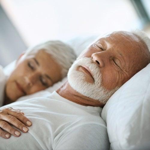 A couple with short white hair sleeps peacefully in bed together