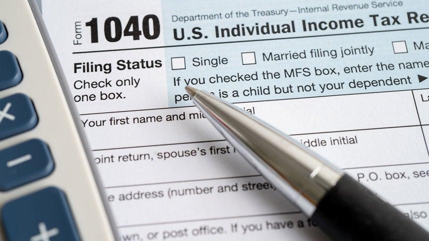 A closeup of a 1040 IRS tax form with a calculator and ballpoint pen close by.