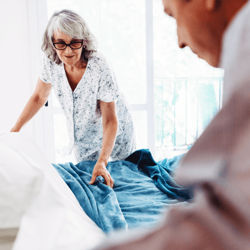 An older woman and man pull the covers back as they prepare to get into bed.