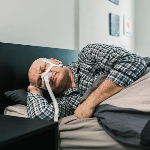 A man lying on his side in bed using a CPAP machine