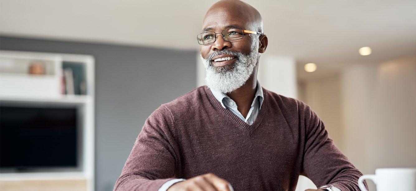A senior black man is smiling, looking away from the camera, thinking about his financial planning choices.