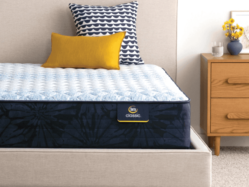 The Serta Classic bed on a beige bedframe next to a wooden nightstand