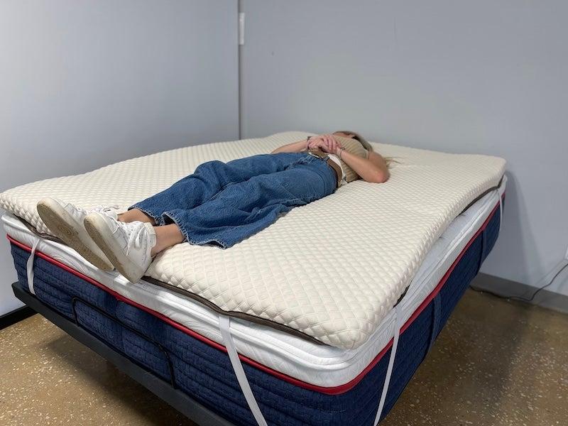 A woman lies on her back on the Nolah mattress topper