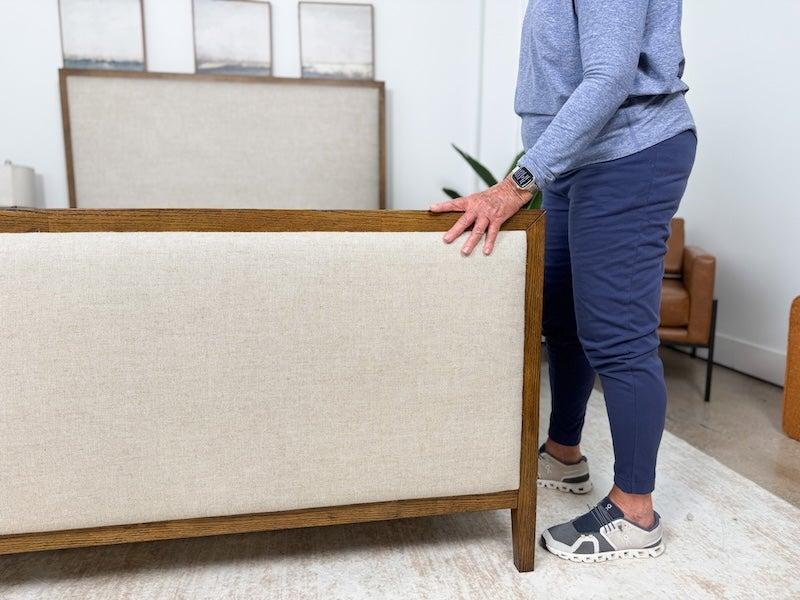 A tester touches the upholstered footboard of the Saatva Calais bed frame