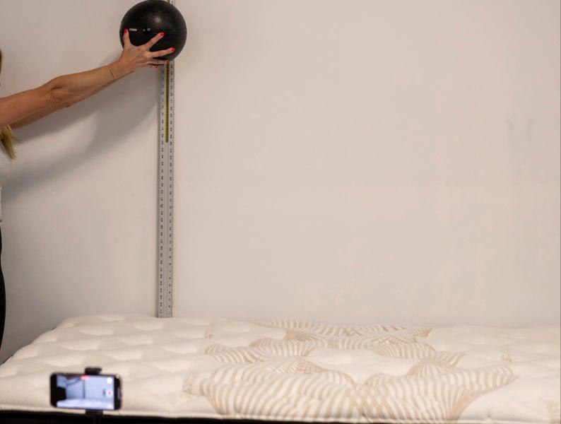 Hands dropping a bowling ball from a height on the Nolah Evolution Luxury Firm mattress to test its bounce.