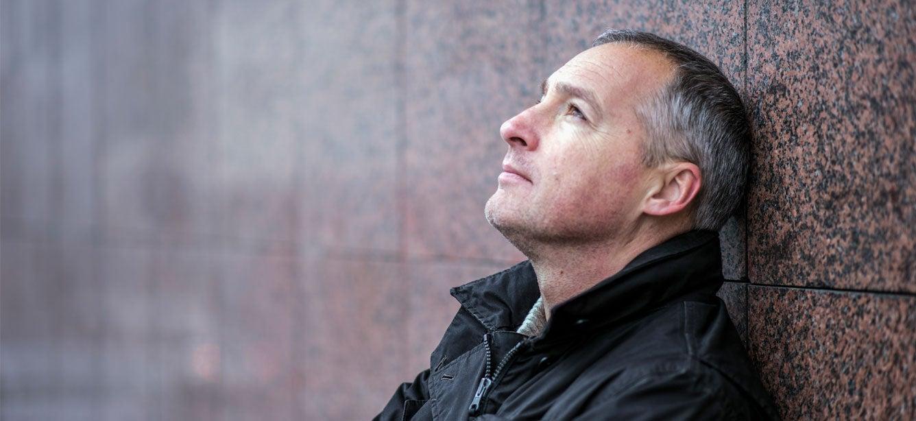 A senior Caucasian man is leaning against a marble wall, contemplating life.
