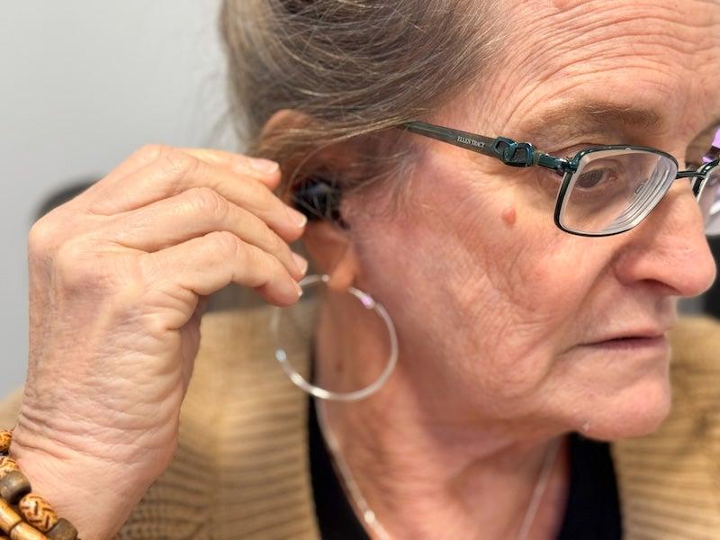 A woman places the Lexie H1 earbud-style hearing aids in her ear