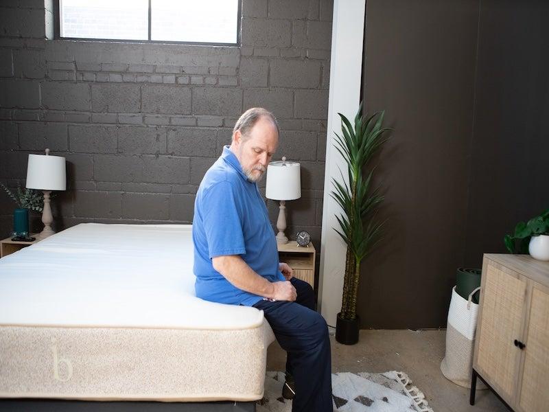 A man sits on the edge of the Birch Natural mattress