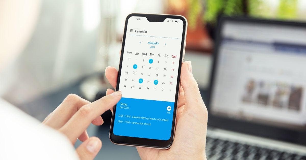 Close up shot of a person holding a cell phone, looking at their calendar trying to make a decision.