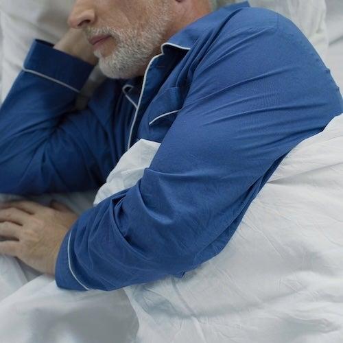 A man in blue pajamas lies on his side in bed
