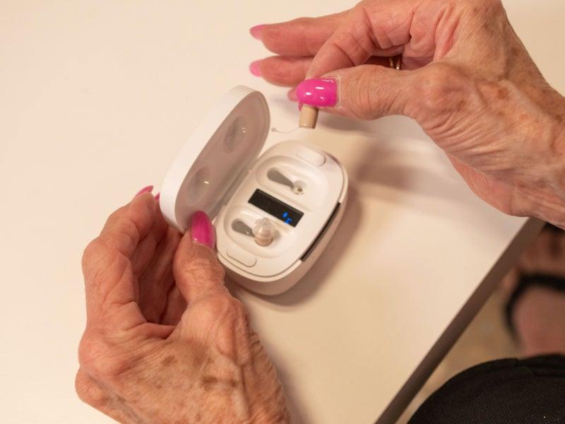 A person's hands removing the Ceretone CoreOne Pro hearing aids from its case