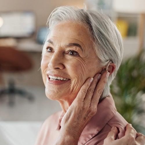 A happy woman touches the hearing aids in her ear