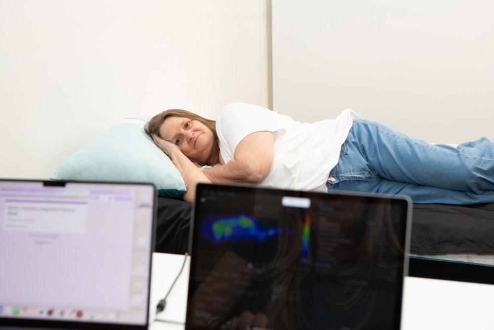 An older woman laying on her side on the Nectar Premier mattress with computers measuring pressure relief in front of her