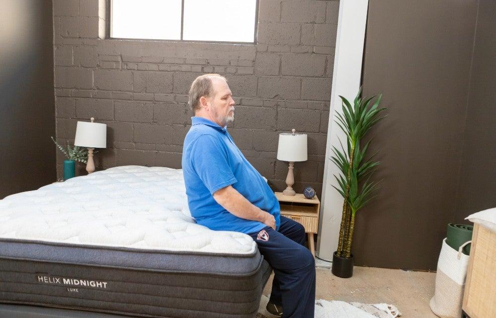 An older man sitting on the edge of the Helix Midnight Luxe mattress