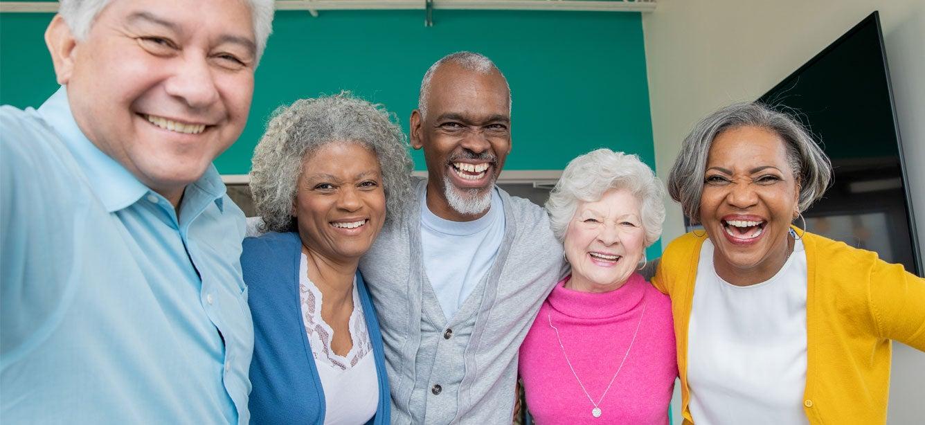 Group of five smiling adults of diverse backgrounds, posing closely together against a colorful background.