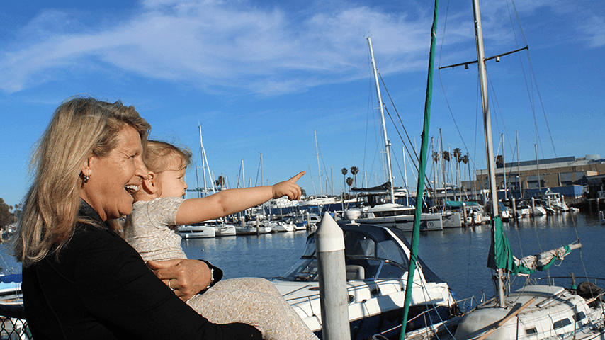 grandmother smiling and holding toddler granddaughter pointing at boats
