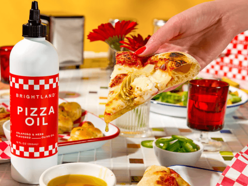 Piece of pizza being dipped into Brightland Pizza Oil.