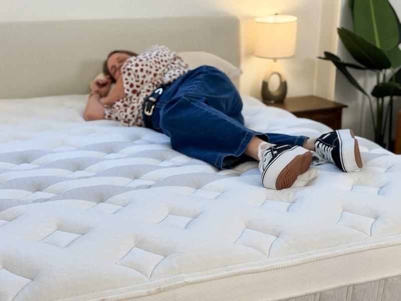 A woman in a blouse and blue jeans rests on her side on the Leesa Sapira Chill mattress