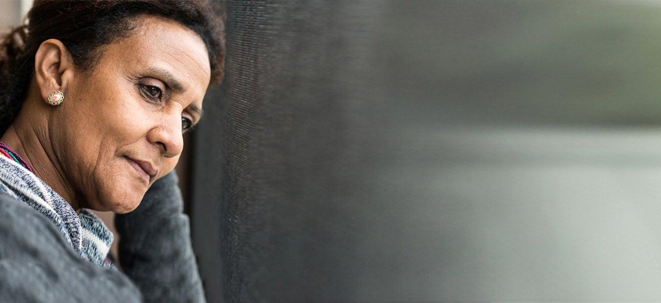 Older Hispanic woman with gray sweater looking sad while gazing out a window