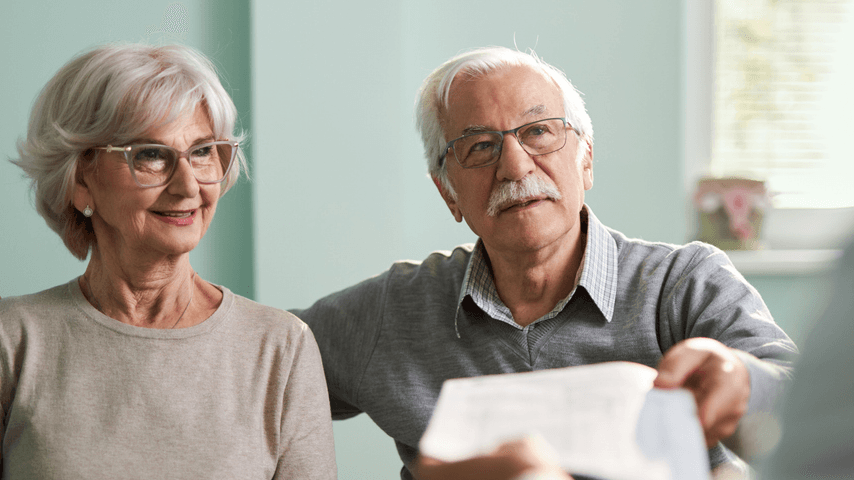 A couple sits at a desk and accepts a piece of paper from someone.