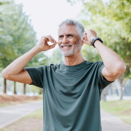 Man with grey hair and a green shirt adjusts his earbuds
