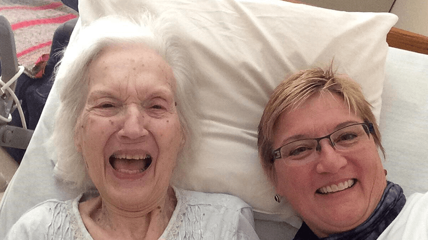 Older woman laughing with younger woman in bed