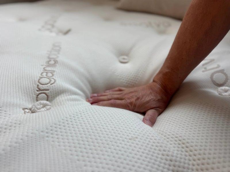 A man’s hand pushes down on the Saatva latex hybrid mattress.