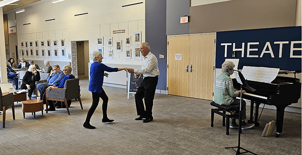 older couple dancing at senior center as volunteer plays piano