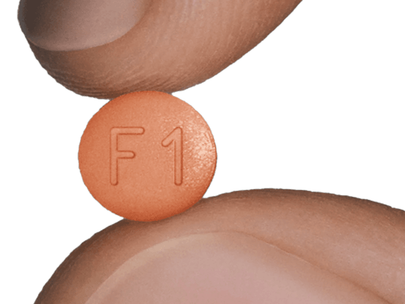 A tablet of Ro Oral Finasteride held between a finger and a thumb