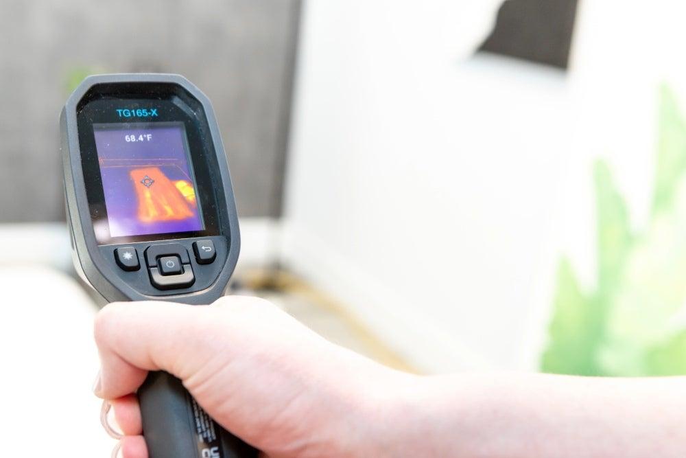 A man points a heat gun at a mattress to measure temperature buildup