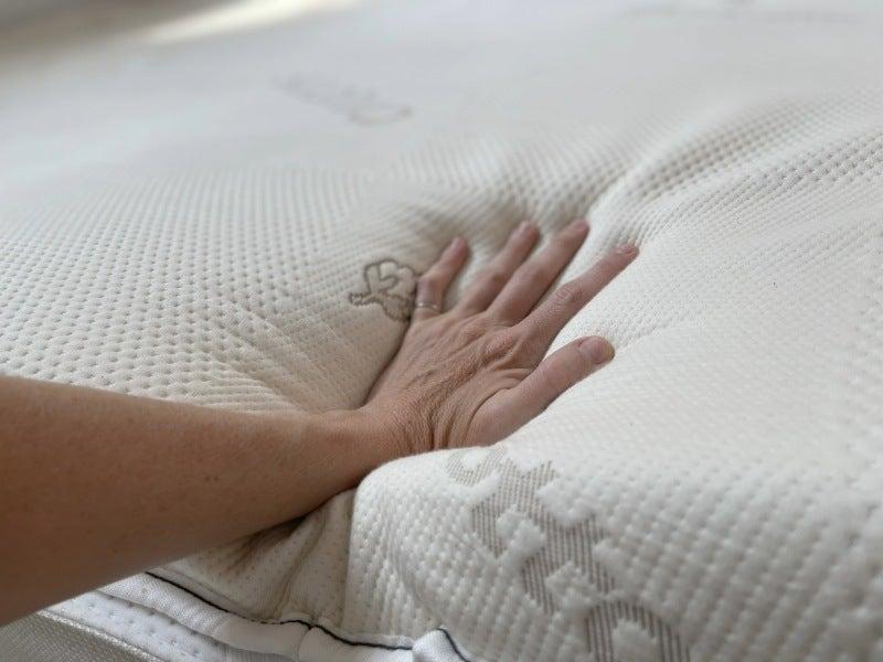 A hand pressing into the Saatva Graphite Memory Foam topper