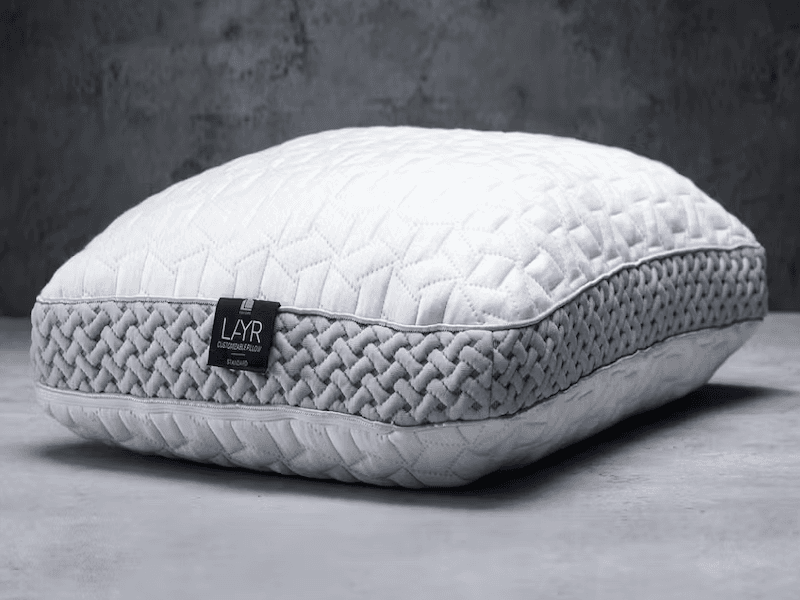 Puffy pillow with white and gray pattern and “LAYR” written on the tag, on a gray background