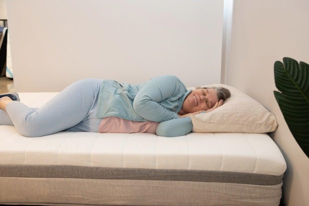 A woman smiles and lies on her side with her eyes closed on a Helix Plus mattress