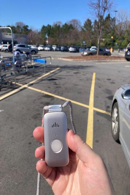 The silver LifeFone VIPx GPS wearable held aloft in a store parking lot