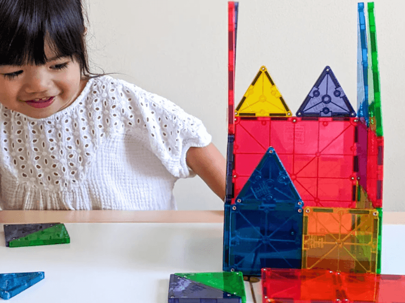 Toddler smiling as she plays with a set of brightly colored Magna_Tiles