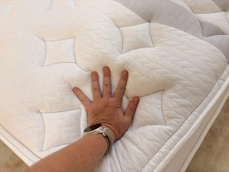 A woman’s hand pressing into the top of the Leesa Sapira Chill hybrid mattress.