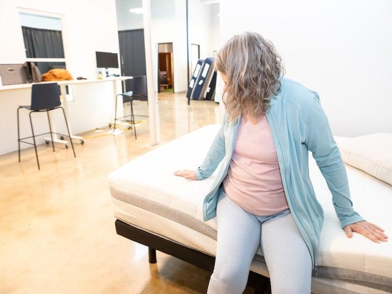 A woman sits on the edge of the Helix Plus mattress to test its edge support.