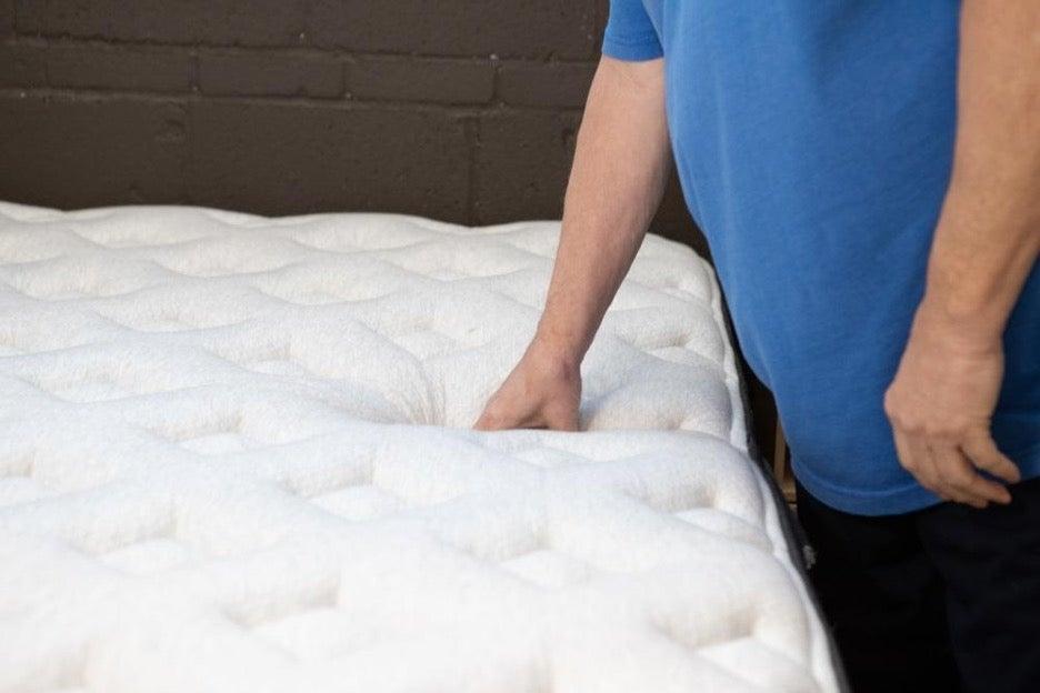 An older male tester pushes down the pillow top of the Helix Midnight Luxe.