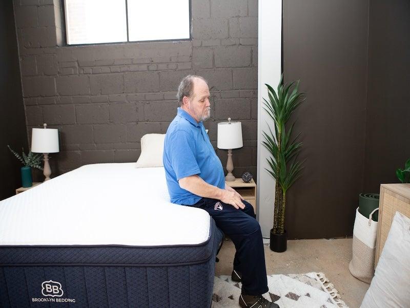 A man sits on the edge of the Brooklyn Bedding Aurora Luxe Cooling mattress.