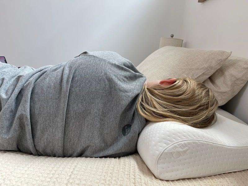 A woman lies on her side on the TEMPUR-Neck pillow