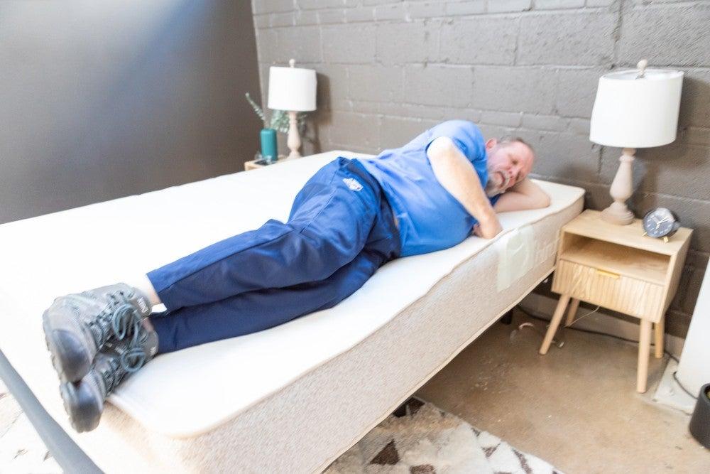 A man lying on his side at the edge of a mattress