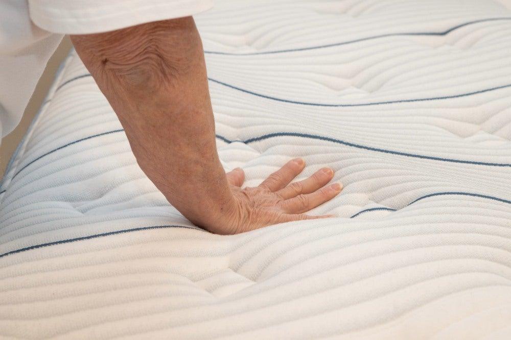 A person holds their hand over the top of a Bear Elite Hybrid mattress