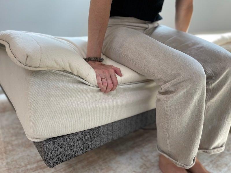 A woman sits on the edge of the Birch Plush Organic mattress topper