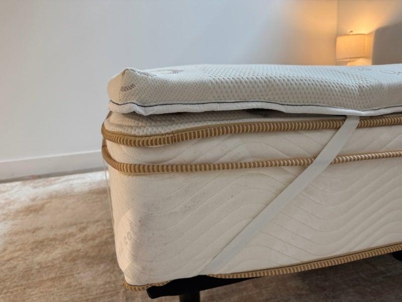 A close up image of the Saatva Natural Latex topper strapped to a bed at the corner