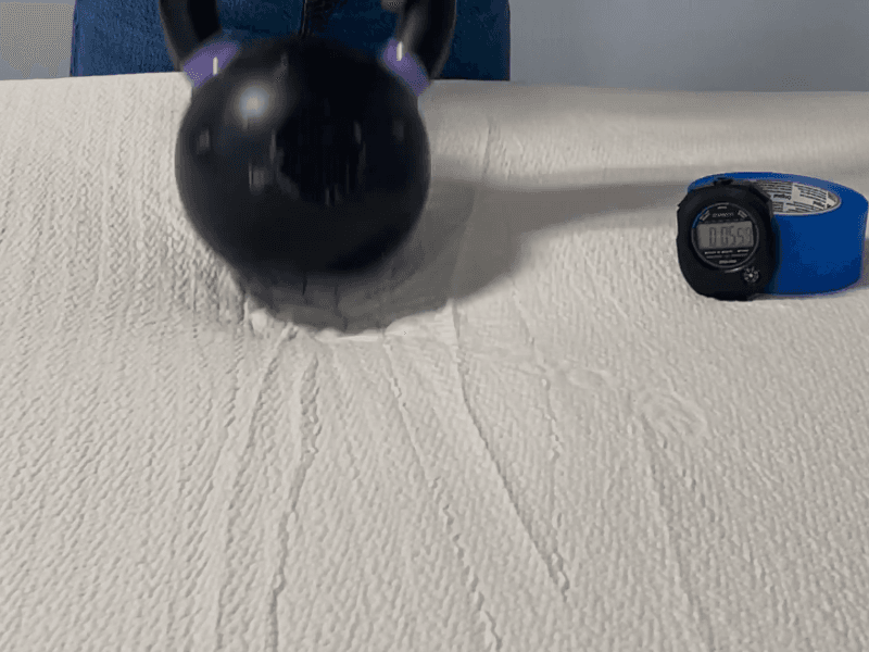 A kettlebell lifting off the Avocado Eco Organic Latex Topper while a stopwatch runs next to it.