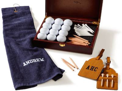 Golf set showing monogrammed golf towel and golf bag tags, and a box containing golf balls, tees, and pencils.