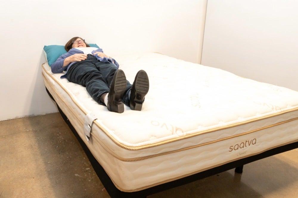 An older adult woman lies on her back on the Saatva Classic Luxury Firm mattress