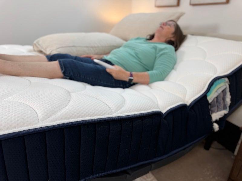 A woman lies on the DreamCloud Hybrid mattress in an adjustable bed with her upper body and legs elevated.